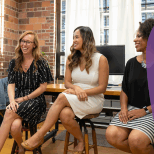 Women sitting on charis stalls in a circle inside a room, chatting and smiling